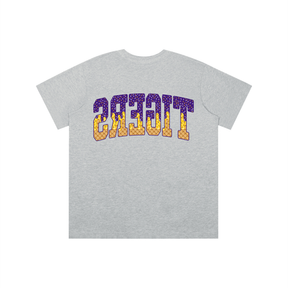 A heather gray short-sleeve t-shirt with a graphic on the chest spelling 'TIGERS' in purple and yellow patterned block letters, shown against a plain white background.