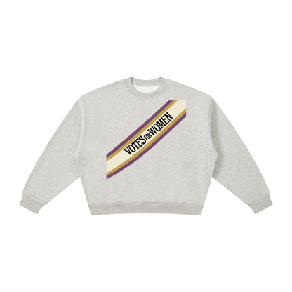 A light heather gray crewneck sweatshirt featuring a diagonal graphic stripe across the chest with the text 'VOTES FOR WOMEN' in black, bordered by purple and cream.