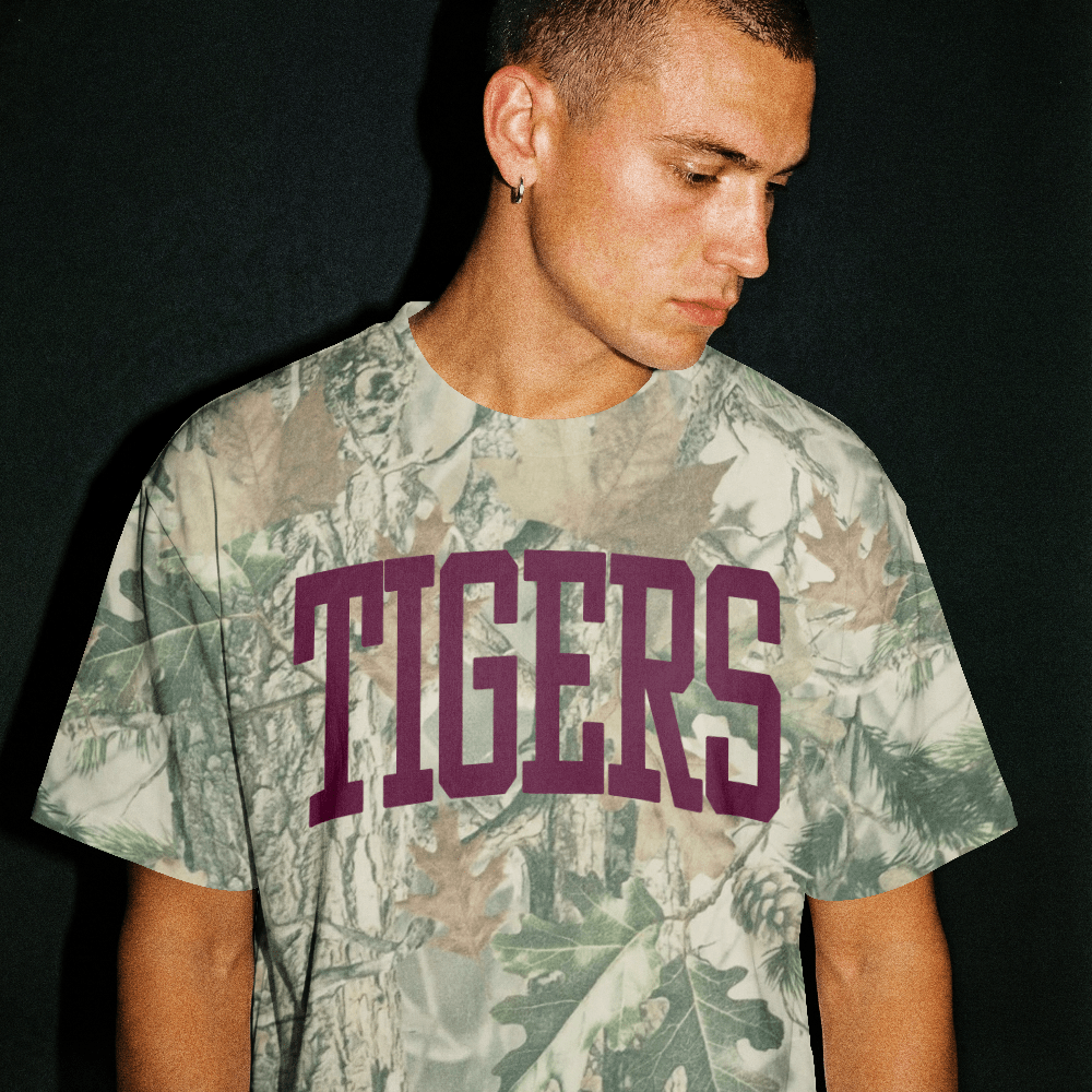 Man wearing oversized camo t-shirt with TIGERS in bold purple letters, streetwear style